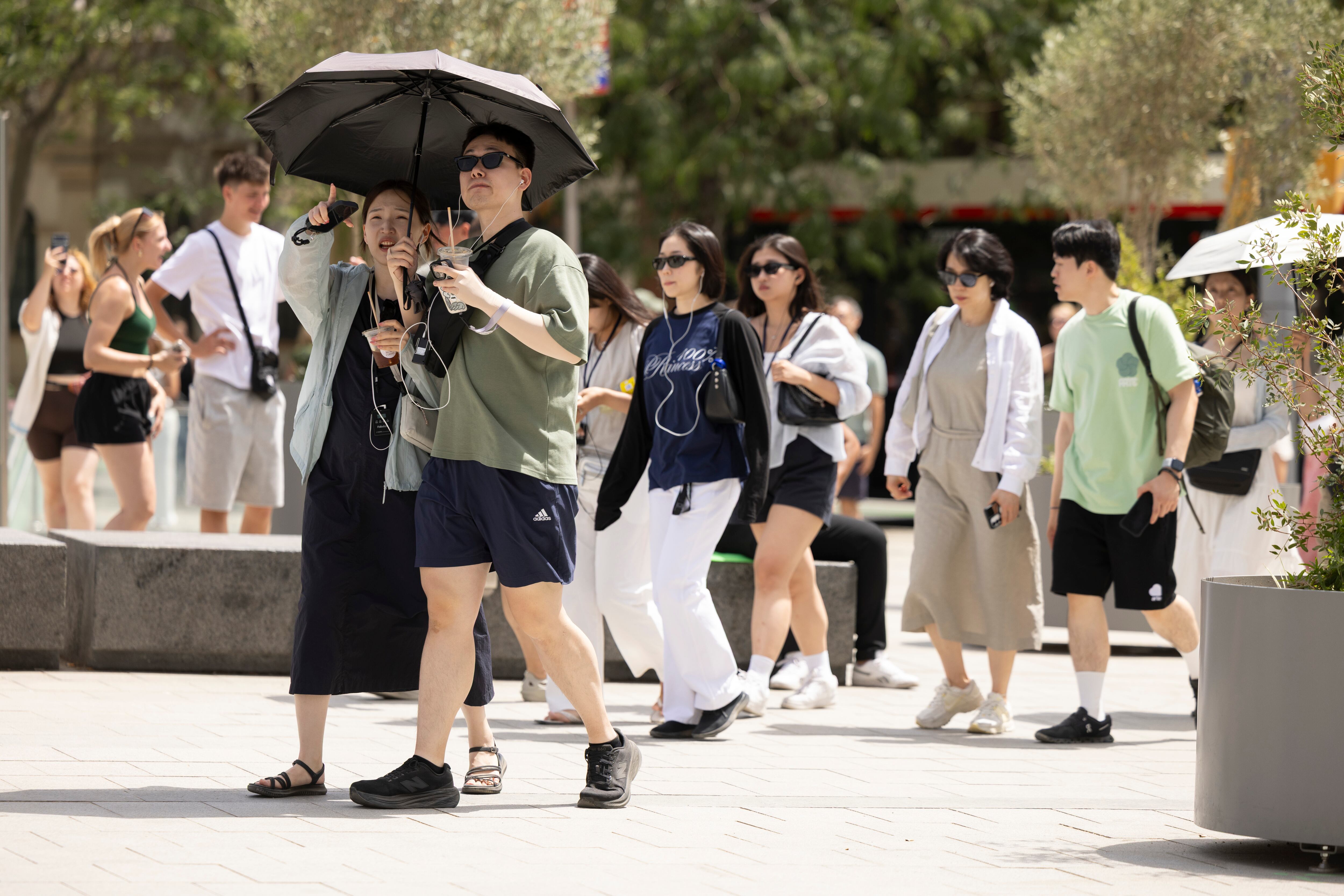 Turistas en las imediaciones de la Sagrada Familia se protegen del calor con paraguas y abanicos.