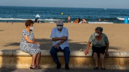 Tres personas mayores descansan en el paseo marítimo de la playa de la Malvarrosa (Valencia).