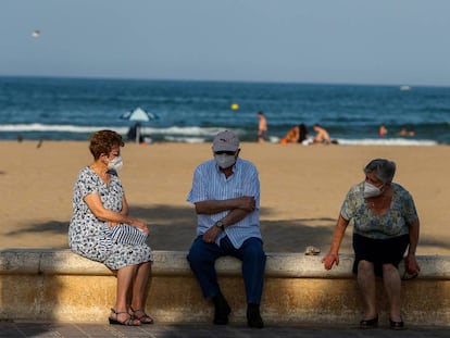 Tres personas mayores descansan en el paseo marítimo de la playa de la Malvarrosa (Valencia).