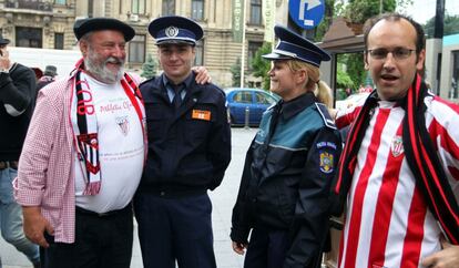 Dos aficionados rojiblancos posan junto a dos policías locales en Bucarest