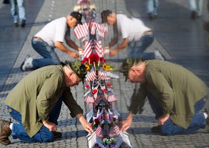 Dos hombres colocan tarjetas y banderas en el muro conmemorativo de los veteranos de Vietnam, en Washington.