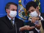 FILE - In this March 18, 2019 file photo, Brazil's Health Minister Luiz Henrique Mandetta, right, gives anti-bacterial gel to President Jair Bolsonaro as they give a press conference on the new coronavirus at Planalto presidential palace in Brasilia, Brazil. Mandetta criticized Bolsonaroâ€™s dismissive handling of the COVID-19 pandemic on national television Sunday night, April 12, and the presidentâ€™s repeated threats to fire him are worrying health experts who say that amid governmental chaos, the health minister's advice to limit contact and take the virus seriously has played a major role in preventing Brazilâ€™s epidemic from being even worse.  (AP Photo/Andre Borges, File )