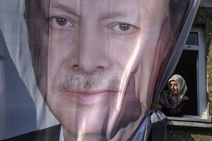 Una mujer mira desde una ventana parcialmente cubierta por un cartel gigante que del presidente turco Recep Tayyip Erdogan, durante un mitin del Partido Justicia y Desarrollo (Partido AK) para las elecciones locales en el distrito de Kasimpasa en Estambul.