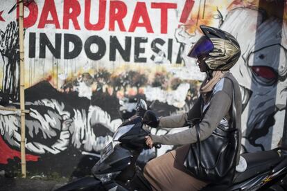 Una motorista en la calzada, delante de uno de los murales del colectivo de X-Go, en una calle de Surabaya, Este de Java, Indonesia. 