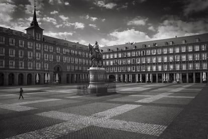 Una persona cruza la solitaria Plaza Mayor de Madrid el primer día del confinamiento. Las sombrillas recogidas son el único recuerdo de las bulliciosas terrazas. Madrid, 15 de marzo de 2020. Fotógrafos como Carmenchu Alemán se lanzaron a la calle aquellas semanas a pesar del riesgo de contagio y el desconocimiento de cómo actuaba el virus.