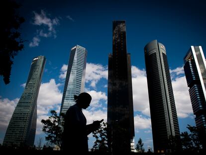 Una mujer, concentrada en la pantalla de su móvil, frente a las torres del distrito financiero de Madrid.