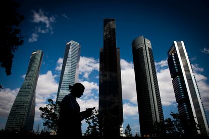 Una mujer, concentrada en la pantalla de su móvil, frente a las torres del distrito financiero de Madrid.