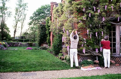 Los decoradores mientras colocan flores artificiales en una enredadera en el exterior de Peppard Cottage para el rodaje de 'Howards End'.