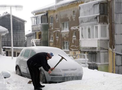 Un hombre rompe el hielo con un pico al lado de un coche cubierto de hielo en Postojna (Eslovenia).