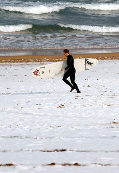 Un surfista se dirige al agua en la playa de Zarautz (Guipúzcoa) tras la intensa nevada de esta mañana.