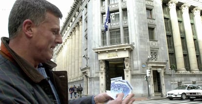 Un hombre muestra unos billetes de 20 euros ante una oficina de BBVA