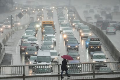 A pedestrian walks with an umbrella as motorists drive through rain along the 110 Freeway in the Hollywood section of Los Angeles, Friday, March 10, 2023.