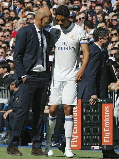 El central francés del Real Madrid Raphael Varane (d) junto al técnico madridista, Zinedine Zidane (i), tras retirarse lesionado del partido.