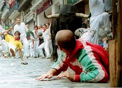 Un mozo, junto al vallado de la curva de Mercaderes con Estafeta, trata de evitar la embestida de un toro durante el último encierro de Sanfermín.