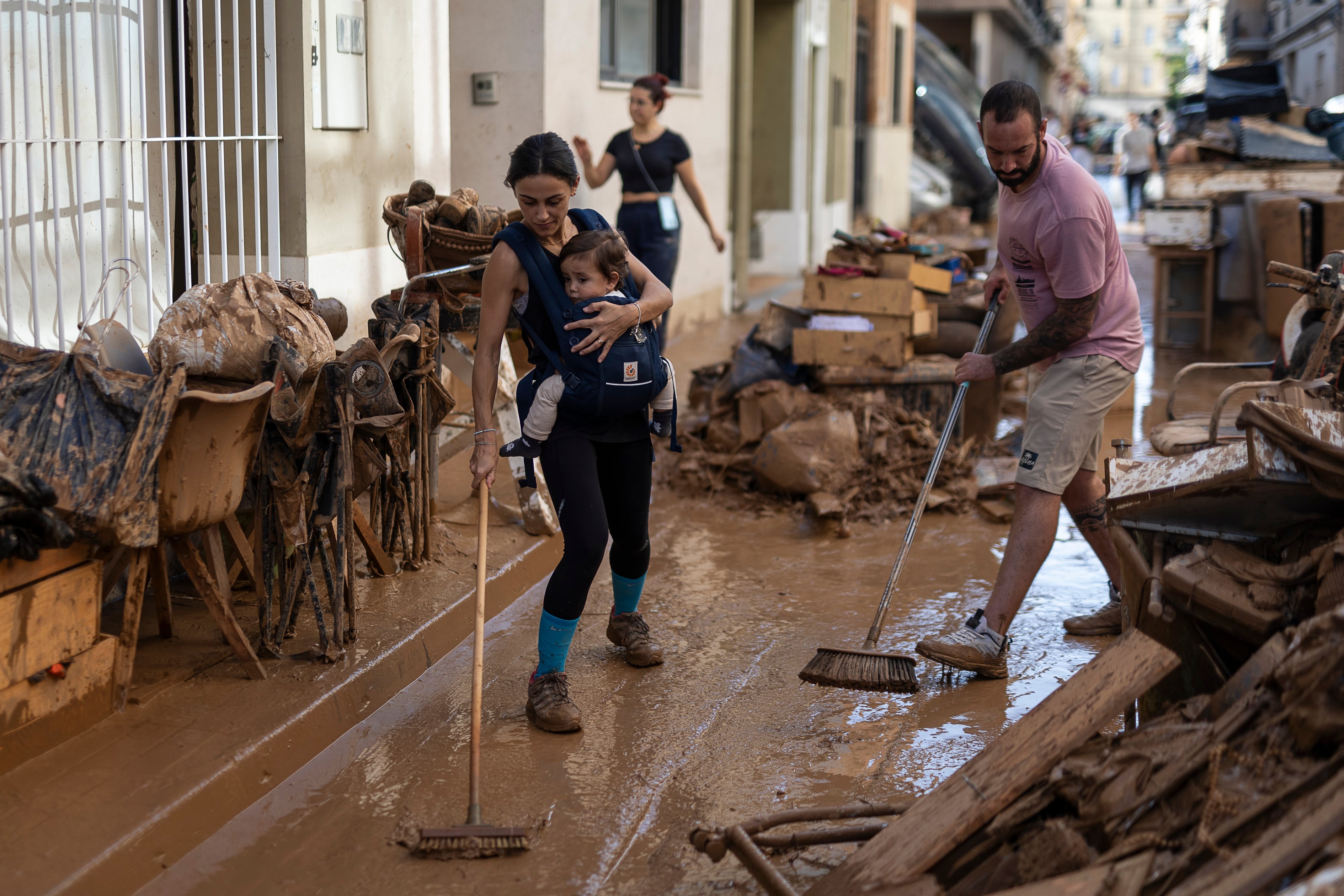 Lorena, vecina de Aldaia, limpia el barro sujetando a su hijo, el jueves en el centro de la localidad.


