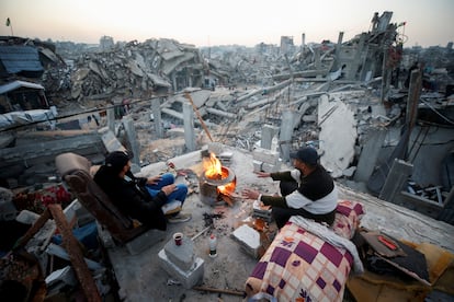 Dos palestinos se calientan en una hoguera entre los escombros de un edificio en Yabalia (Gaza), este lunes. 