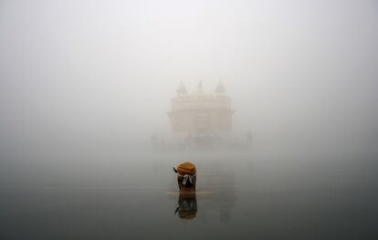 Un devoto Sikh se da un baño en un estanque sagrado del Templo Dorado, santuario Sikh, en medio de una espesa niebla en Amritsar, India.