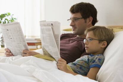 Un padre y su hijo leen el periódico en la cama.