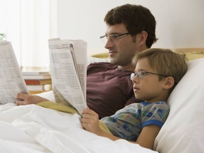 Un padre y su hijo leen el periódico en la cama.