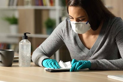 Una mujer desinfecta su móvil con guantes y mascarillas.