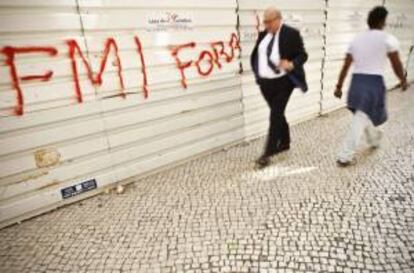 Personas pasan frente a una pintada que dice "FMI, fuera!", en Lisboa, Portugal. EFE/Archivo