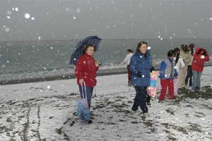 Varias personas recorren esta mañana la playa de Motril, cubierta de nieve.