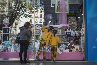 Una niña mira el escaparate de una tienda de juguetes en una calle comercial del centro de Sevilla.