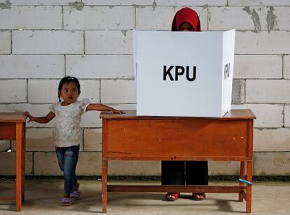 Una niña está de pie junto a una mujer que vota durante las elecciones en Bogor, Java Occidental.