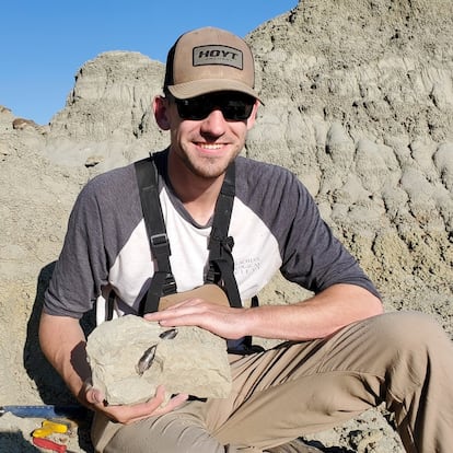 El científico Jared Voris,realiza trabajo de campo sosteniendo una roca que contiene un diente de tiranosaurio.