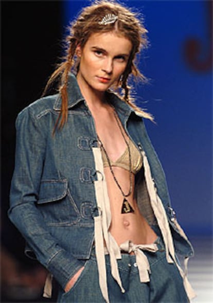 Pantalón y chaqueta en denim con arandelas y cintas como botones, que dejam ver un sujetador dorado, un diseño de la colección primavera-verano 2005 de Jocomomola.