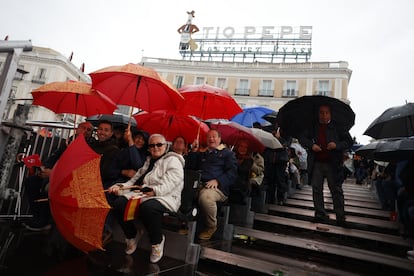 Ciudadanos se protegen de la lluvia, durante el acto institucional este viernes en la Puerta del Sol de Madrid.