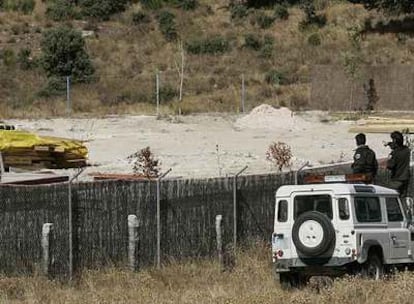 Unos agentes forestales vigilan el interior de una finca desde la valla exterior.