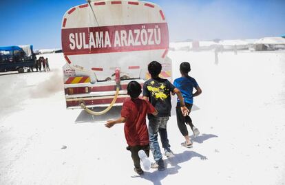 Tres niños refugiados corren tras un camión de agua en el campamento temporal de la localidad de Ain Issa, próxima a Raqqa (Siria).