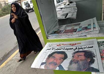 Una mujer iraquí camina por las calles de Bagdad junto a un puesto de prensa, donde se destaca la detención de Sadam.