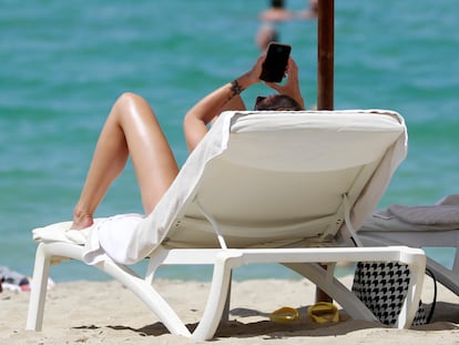 Una mujer consulta su móvil mientras toma el sol en una playa de Mallorca en 2022.