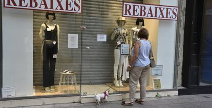 Una mujer observa el escaparate una tienda en rebajas cerrada. 