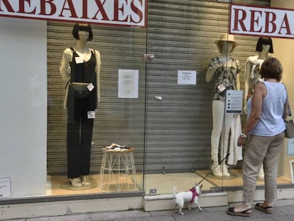 Una mujer observa el escaparate una tienda en rebajas cerrada. 