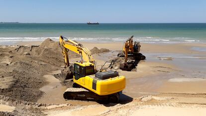 Unas máquinas excavadoras retirando arena de la playa de en Cádiz, en Andalucía.