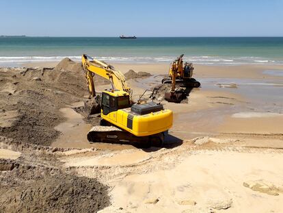 Unas máquinas excavadoras retirando arena de la playa de en Cádiz, en Andalucía.