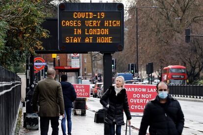 Um grupo de pessoas caminha por uma rua de Londres em que um painel alerta sobre o alto risco de contágio na cidade.