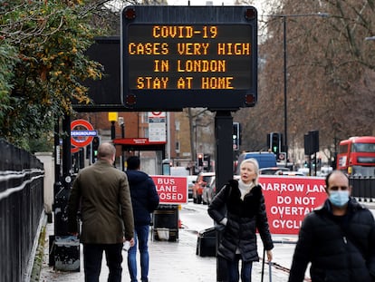 Un grupo de personas camina por una calle de Londres en la que un cartel luminoso advierte del alto riesgo de contagio en la ciudad.