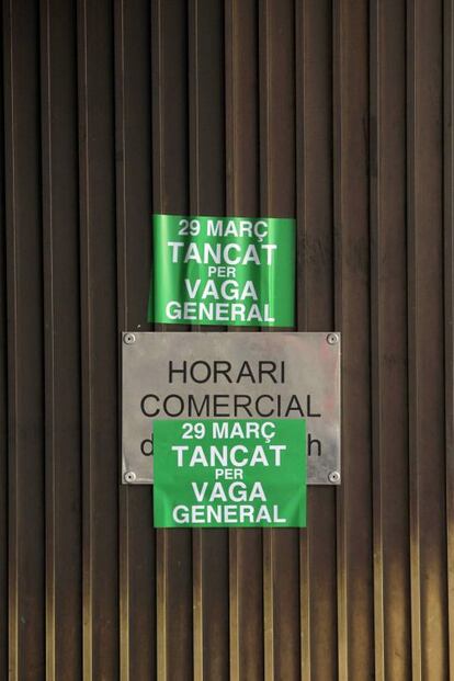 Detalle del cartel con el horario comercial de unos grandes almacenes del centro de Barcelona tapado con carteles llamando a la huelga general.