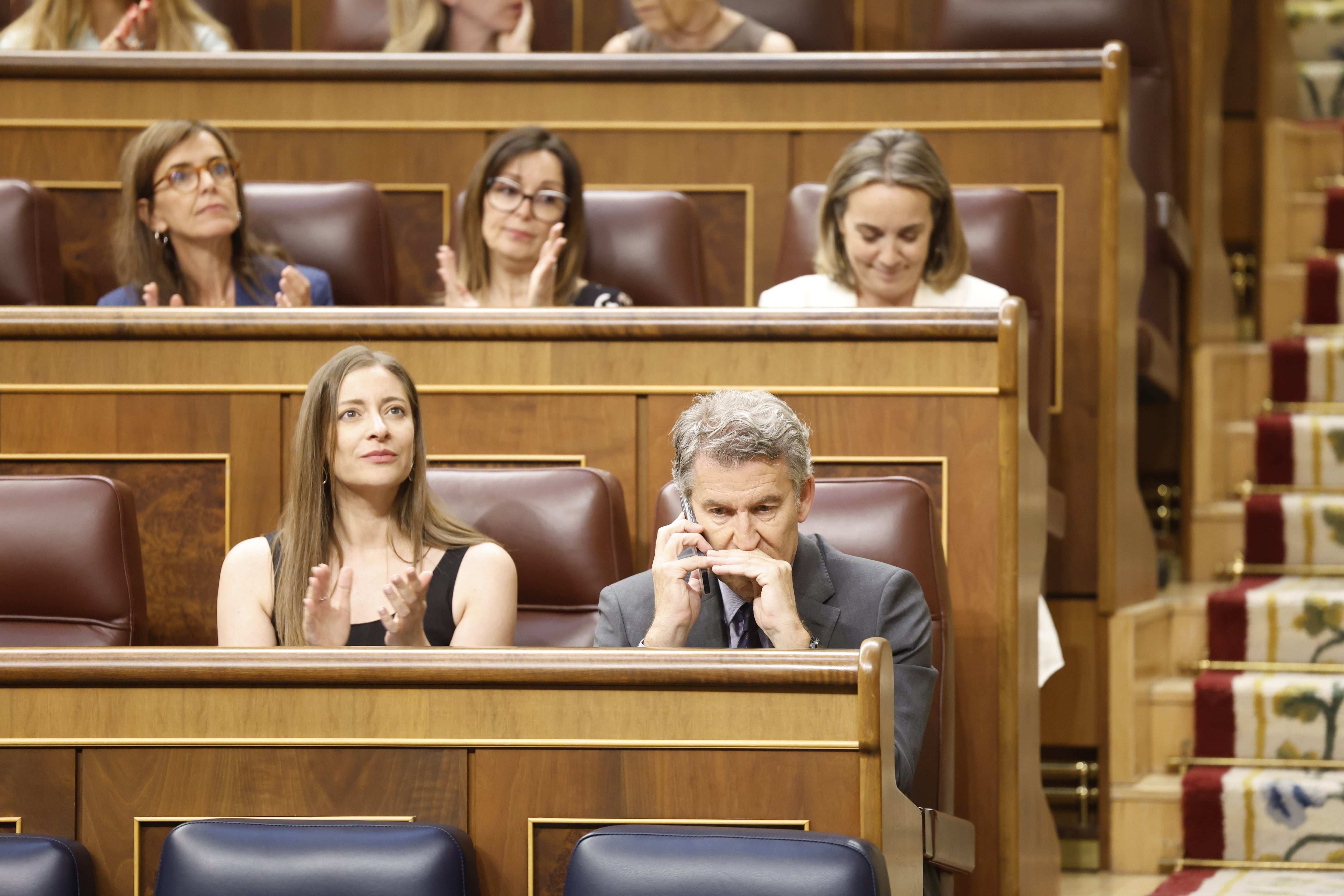 El líder del PP, Alberto Núñez Feijóo, habla por teléfono junto a su portavoz en el Congreso, Ester Muñoz, durante la sesión plenaria del Congreso celebrada este jueves. 