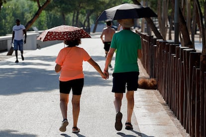 Una pareja pasea protegida por paraguas para mitigar el calor en Madrid. 
