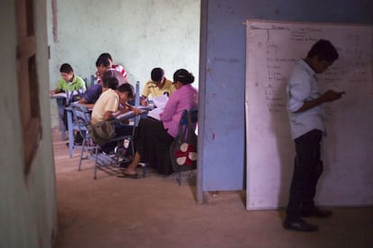 Un grupo de secundaria hace sus tareas mientras otro estudiante atiende su móvil fuera del aula.