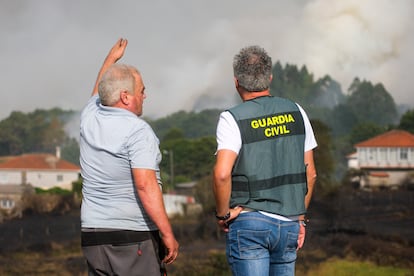 Un vecino habla con un agente de la Guardia Civil en las labores de extinción del incendio que se ha declarado este martes en Dozón, Pontevedra.