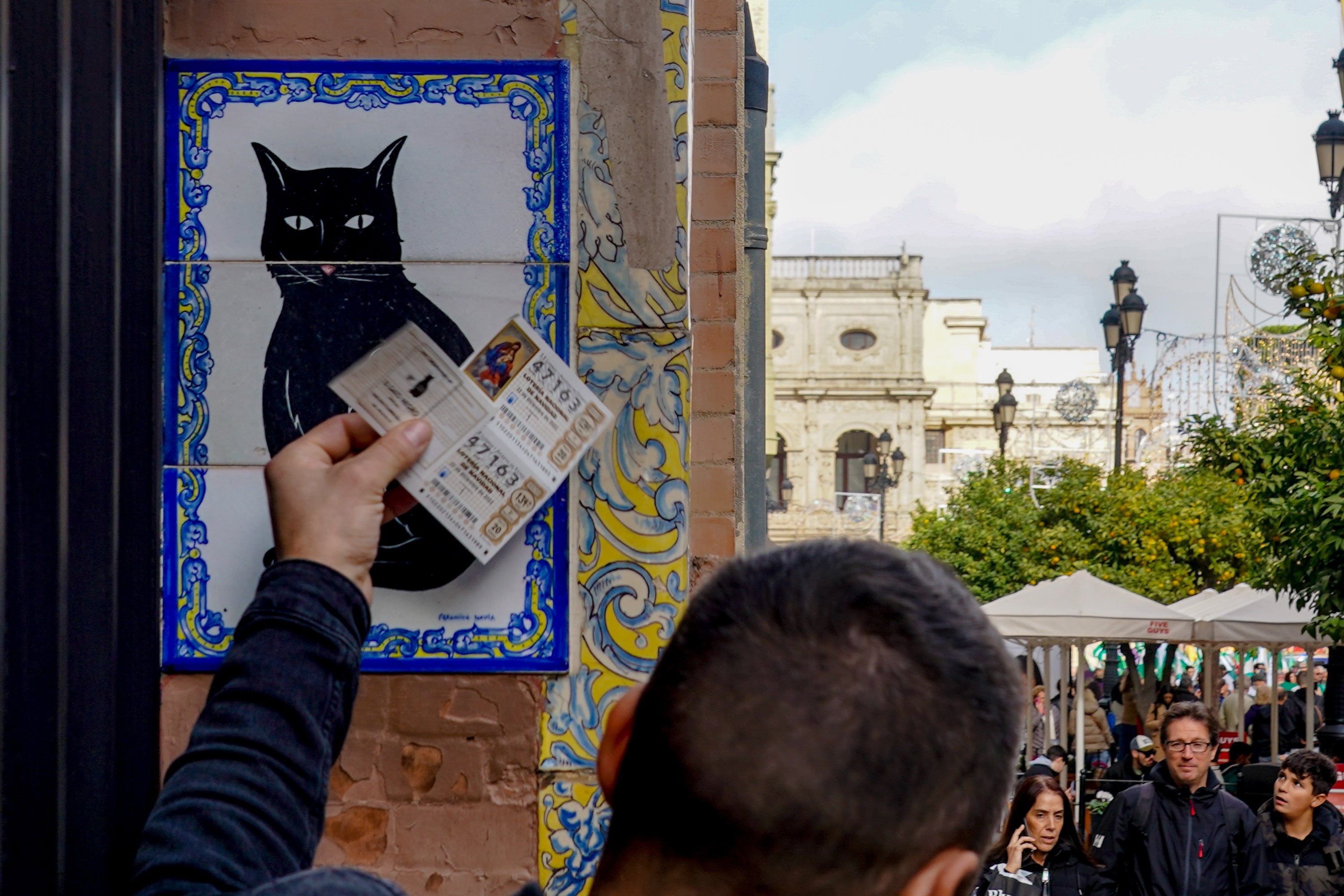 Una persona pone el décimo recién comprado en el azulejo que representa a el gato negro en la administración de loterías ‘El Gato Negro’ situada en la Av de la Constitución para comprar la Lotería de Navidad a 07 de diciembre del 2022 en Sevilla (Andalucía, España). 