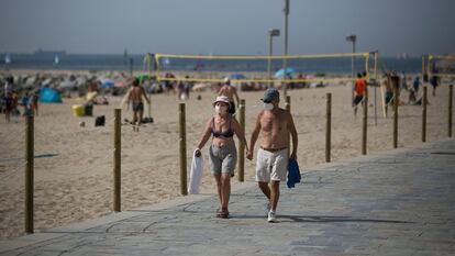 Un pareja camina sin camisetas  y con mascarillas por el paseo marítimo de Barcelona