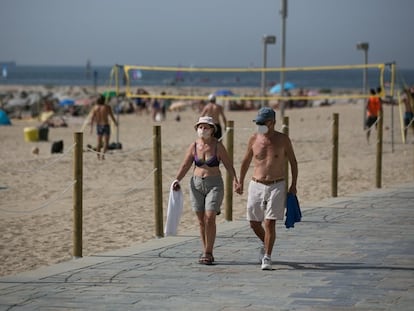Un pareja camina sin camisetas  y con mascarillas por el paseo marítimo de Barcelona