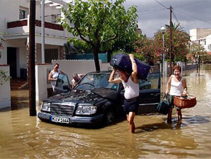 Una familia extranjera intenta extraer sus pertenencias del vehículo en una calle de Coma-ruga inundada por la lluvia.